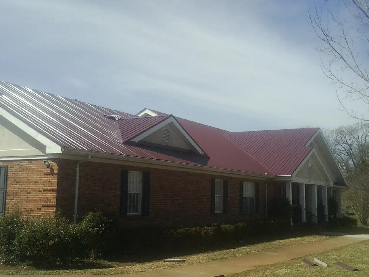 Red metal roof with gabled entries on a long brick building, from a Hail Damage Roof Repair job in Wapato