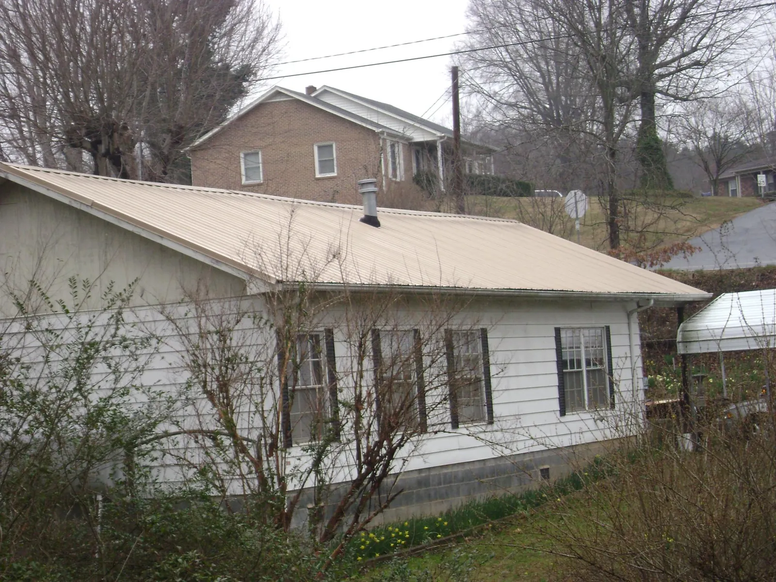 Tan metal roof on a white sided house set into a hillside — Commercial Roofing by Roofing Brothers in Wapato